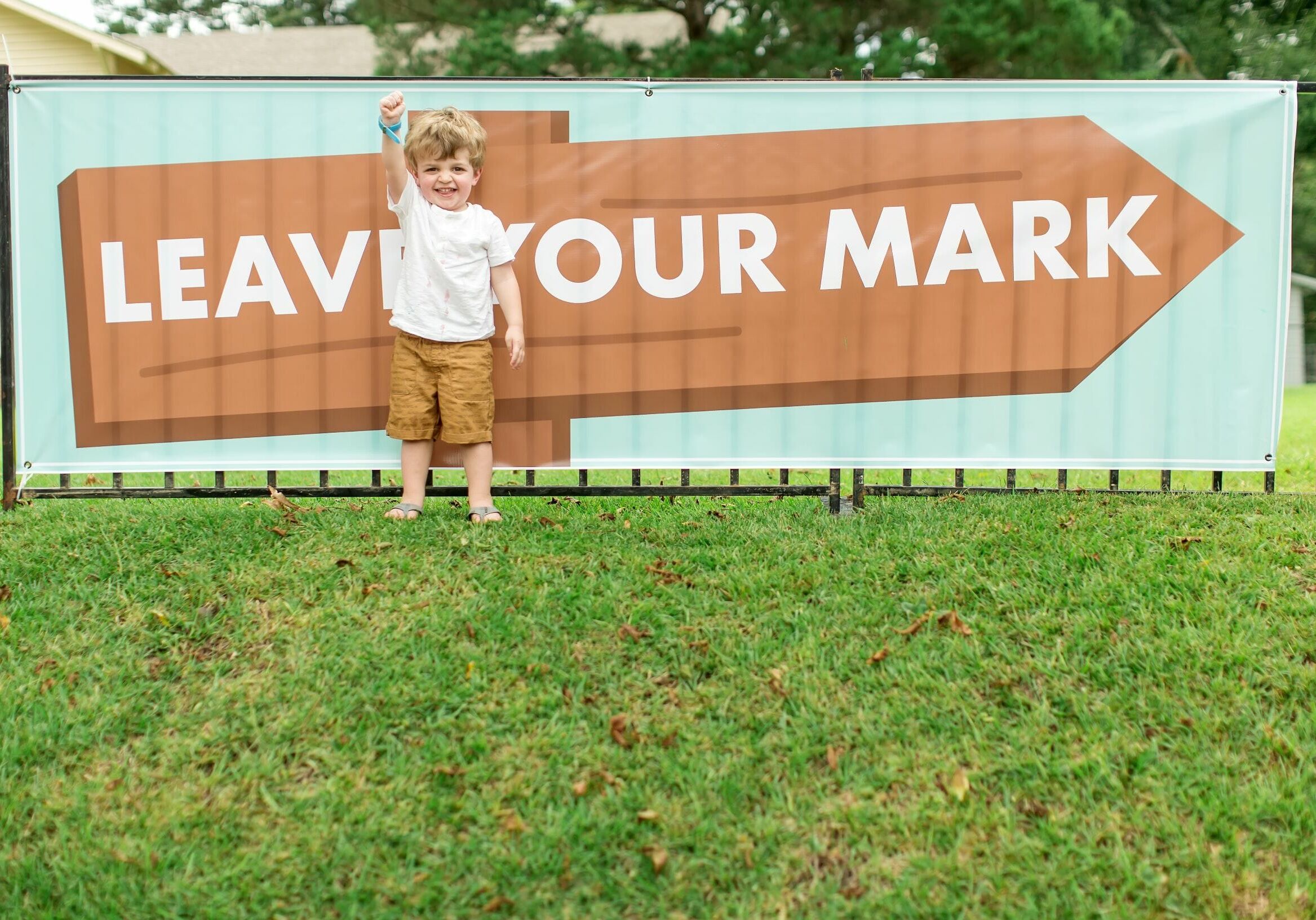 A little boy raising his fist in front of a sign that reads “Leave Your Mark”